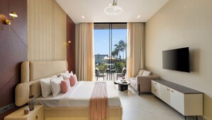 Una habitación de hotel moderna con una cama grande, un televisor de pantalla plana, un balcón con mobiliario para exteriores y un ventilador de techo.
