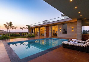 A modern pool area with a clear pool, lounge chairs, and a well-lit building with large windows. - House of Tvara by ELIVAAS (Taoru)