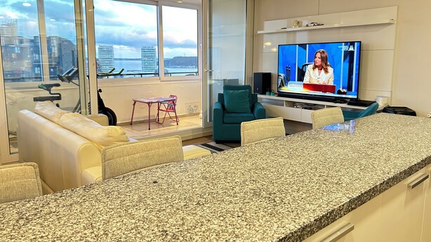 Ein modernes Wohnzimmer mit großem Fernseher, einer Couch, einem kleinen Tisch und einem Sessel.