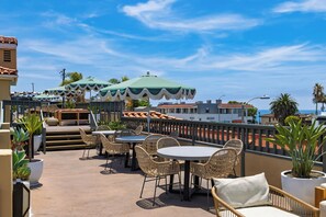 Eine Terrasse im Freien mit Korbmöbeln, Sonnenschirmen und Pflanzen in Töpfen.