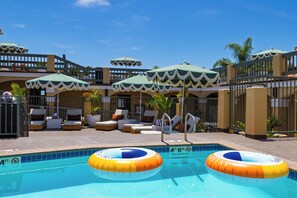 Zona de piscina con sillones reclinables, sombrillas y una piscina con dos anillos inflables.