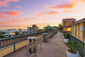 Una terraza en la azotea con mobiliario exterior, vistas al océano y un cielo al atardecer.
