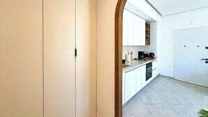 Une cuisine moderne avec des meubles blancs, une machine à café et une vue sur la salle à manger, accessible par une arche.