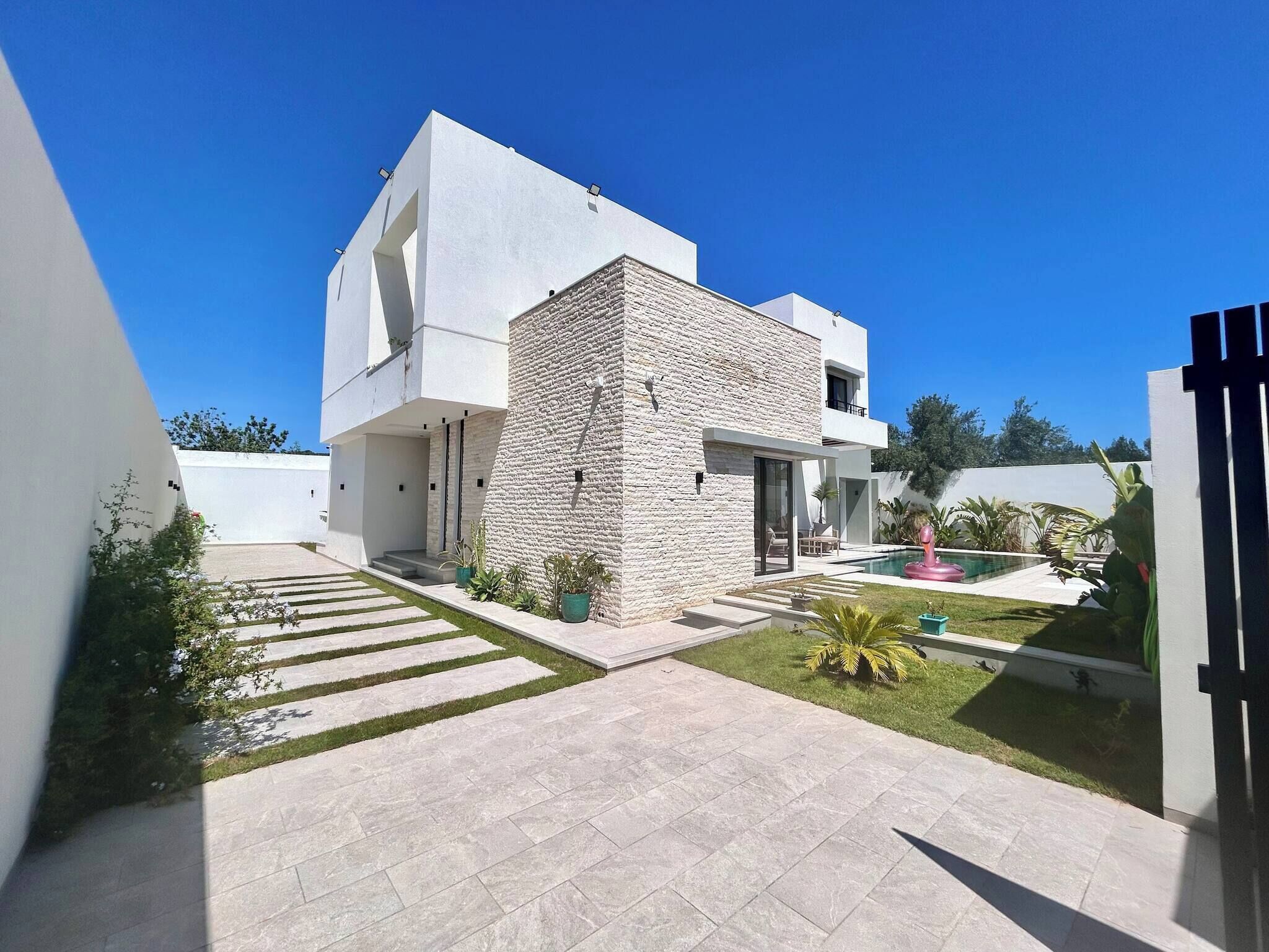 A modern two-story house with a stone facade, a swimming pool, and a well-maintained garden.