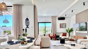 Una sala moderna con comedor, ventanas amplias y televisor de pantalla plana.