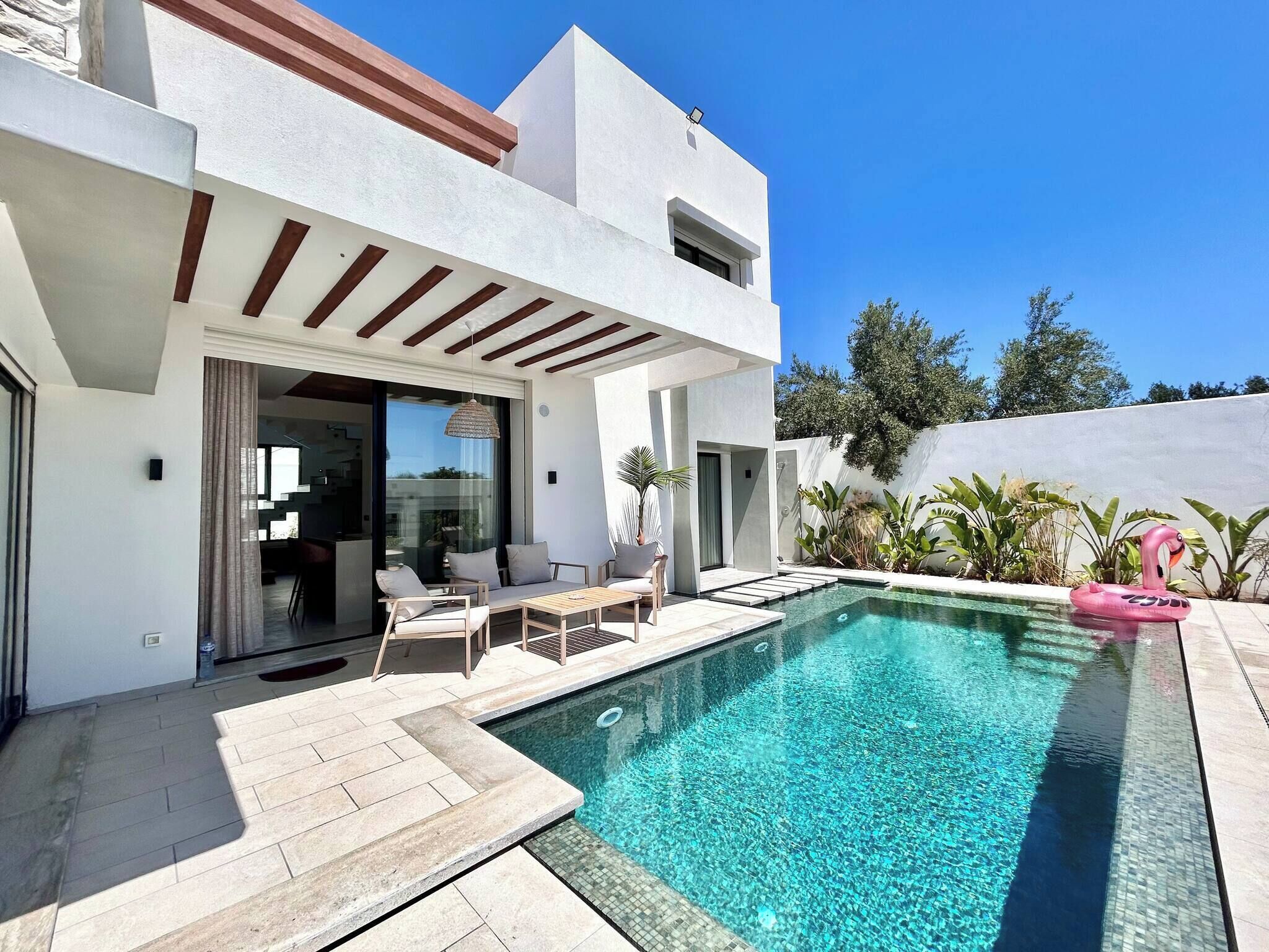 A modern house with a swimming pool, outdoor seating, and a pink flamingo float.