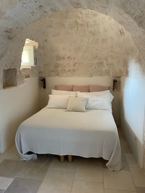 Ein Schlafzimmer mit Steindecke, einem Bett mit weißer Bettwäsche und einem kleinen Fenster.