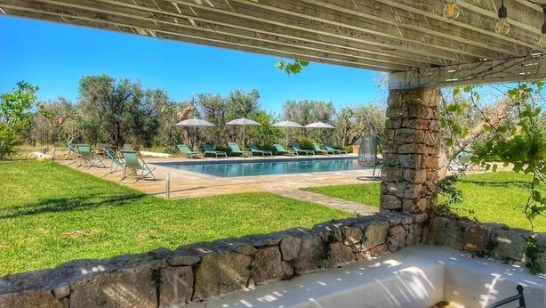 A pool area with lounge chairs and umbrellas, a stone wall, and a clear view of the pool. - Olivi estate with private pool in Ceglie 2 and 4/6/8 pax (Ceglie Messapica)