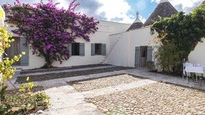 A courtyard with cobblestone flooring, a staircase, and a building with a conical roof. - Olivi estate with private pool in Ceglie 2 and 4/6/8 pax (Ceglie Messapica)