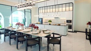 Une cuisine moderne dotée d’un îlot central, d’un coin repas avec une longue table et des chaises, et offrant une vue sur l’extérieur.
