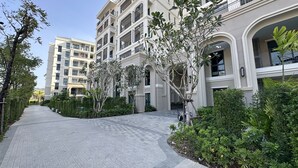 Un immeuble résidentiel à plusieurs étages, doté d’un chemin piétonnier pavé, d’espaces verts et surplombant un ciel dégagé.