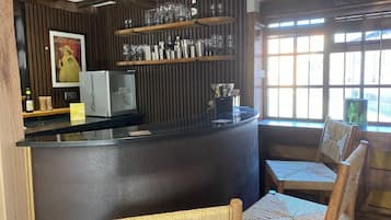 Un espace bar avec un comptoir, des étagères remplies de verres, des chaises en osier et une affiche accrochée au mur.