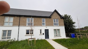 A two-story residential building with a white facade, a dark roof, and a small front yard with a pathway leading to the entrance. - Serene 3-Bedroom House in Athlone (Athlone)