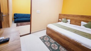 A bedroom with a bed, a blue sofa, a wooden desk, and a patterned rug.