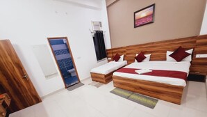 A hotel room with a wooden bed, a small table, a chair, a window with curtains, and a wall-mounted air conditioner.