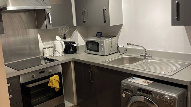 Una cucina compatta con forno integrato, microonde e lavatrice, dotata di elettrodomestici in acciaio inossidabile e un design moderno.