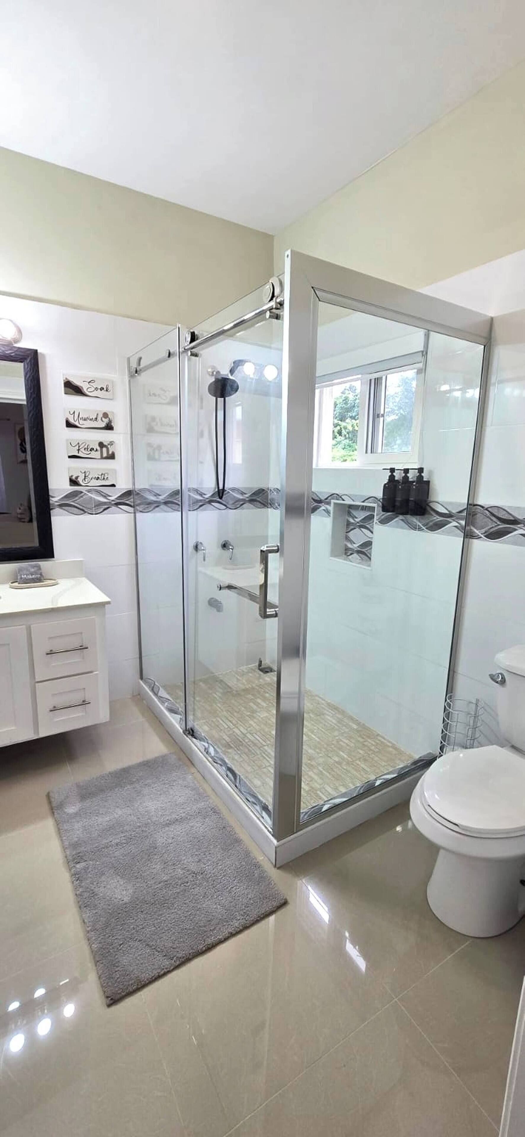 Une salle de bain moderne avec une douche à parois de verre, des toilettes, un meuble-lavabo avec des tiroirs et un miroir.