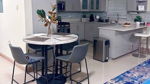 A modern kitchen with white cabinets, a round dining table with four chairs, a clock on the wall, and a blue patterned rug. - Island VYB Luxe Villa Ochi Rios With SOLAR system (Ocho Rios)