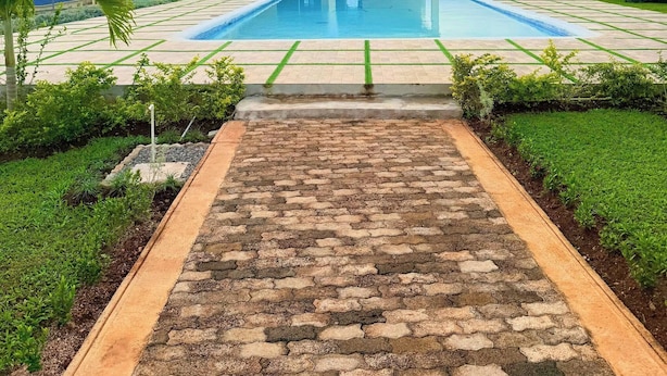 A swimming pool with a paved walkway leading to a building with a dark roof. - Island VYB Luxe Villa Ochi Rios With SOLAR system (Ocho Rios)