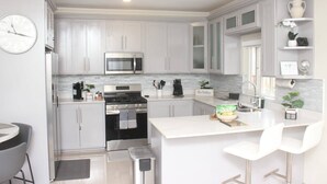 A modern kitchen with white cabinetry, a built-in microwave, an oven, and a large island with bar stools. - Island VYB Luxe Villa Ochi Rios With SOLAR system (Ocho Rios)