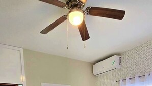 A bedroom with a bed, a ceiling fan, an air conditioning unit, a window with curtains, and a door leading to a bathroom. - Island VYB Luxe Villa Ochi Rios With SOLAR system (Ocho Rios)