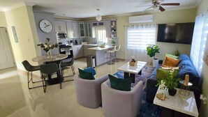 A modern kitchen with a dining area, a living room with a sofa and ottomans, and a TV mounted on the wall. - Island VYB Luxe Villa Ochi Rios With SOLAR system (Ocho Rios)