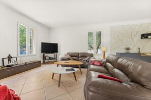 Ein modernes Wohnzimmer mit einer Couch, einem Couchtisch, einem Fernseher und großen Fenstern.