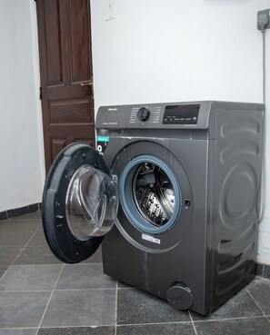Eine Hisense Waschmaschine mit Frontlader und Bedienfeld, vor einer gefliesten Bodenfläche und einer Holztür.
