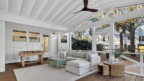 Eine überdachte Veranda mit weißer Decke, Holzboden, einem weißen Sofa, einem Couchtisch und einem kleinen Tisch mit Büchern.