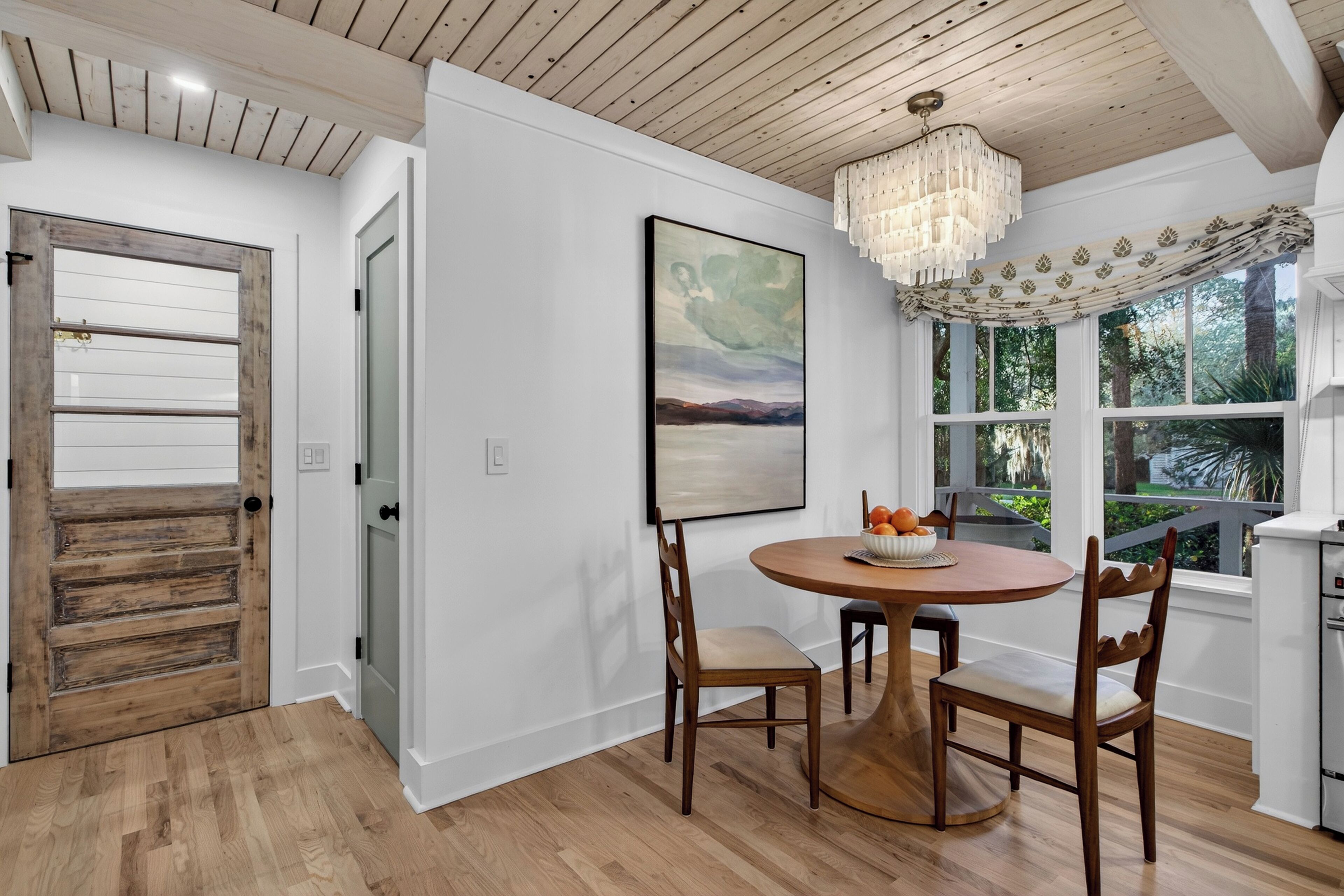 A dining area with a wooden table and chairs, a chandelier, and a painting on the wall.