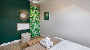 Quarto com cama, luminária pendente, parede verde, espelho emoldurado, quadro e cortina estampada.