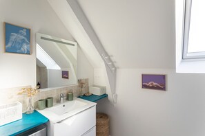 Ein Badezimmer mit einem weißen Waschbecken, einem Spiegel, einer blauen Arbeitsplatte und einer schrägen Decke.