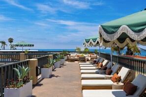 A rooftop lounge area with outdoor seating, potted plants, and a view of the ocean.