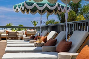 A row of sun loungers with a table and umbrella, a wicker chair, and a railing. - Ocean Views + Pool + Hot Tub| Walk to Beach + Laguna Attractions + Dining (Laguna Beach)