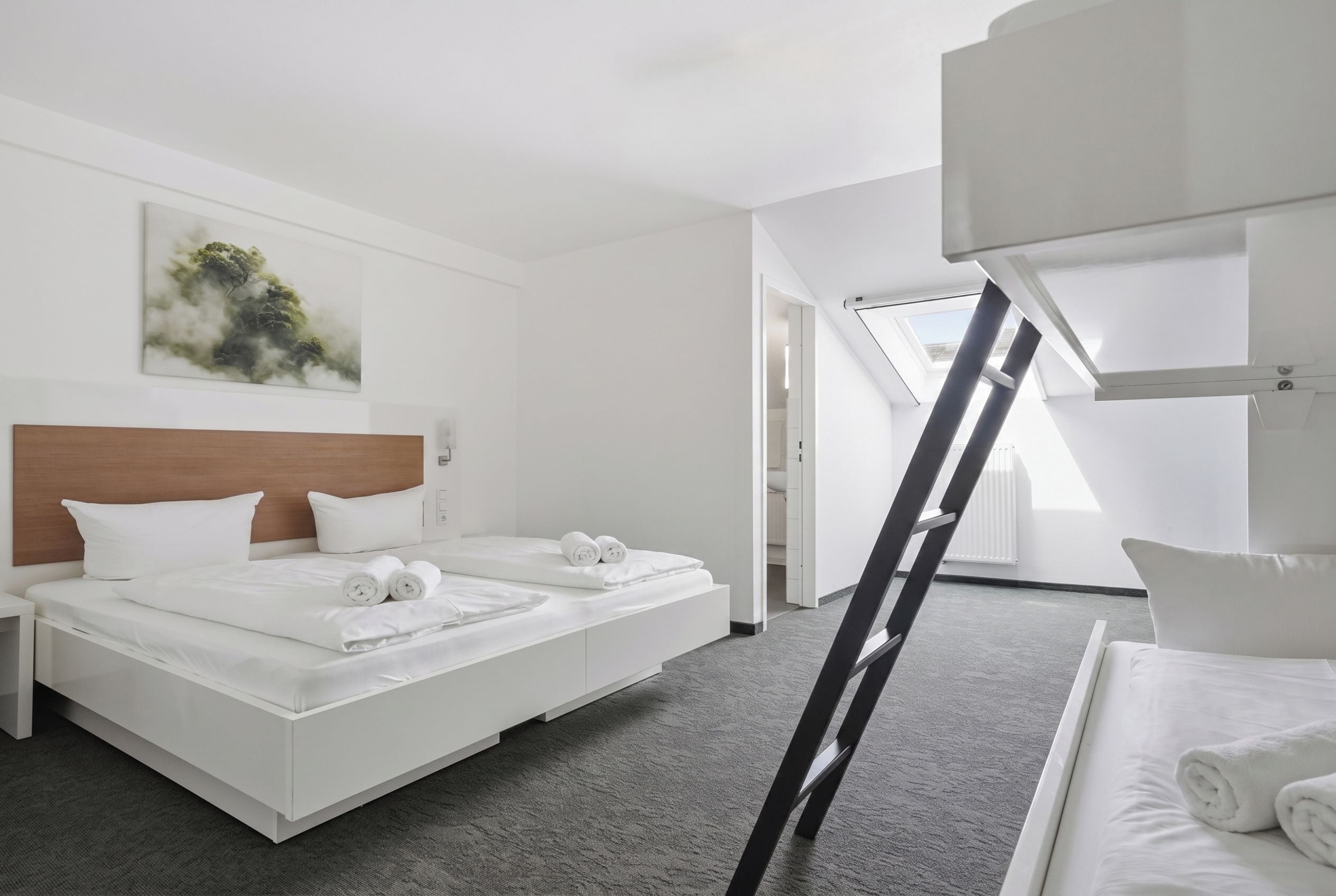 Una camera d'albergo moderna con un letto grande, una testiera, un quadro al muro e un lucernario.