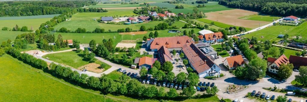 An aerial view of a rural area with a large building complex surrounded by green fields and trees.