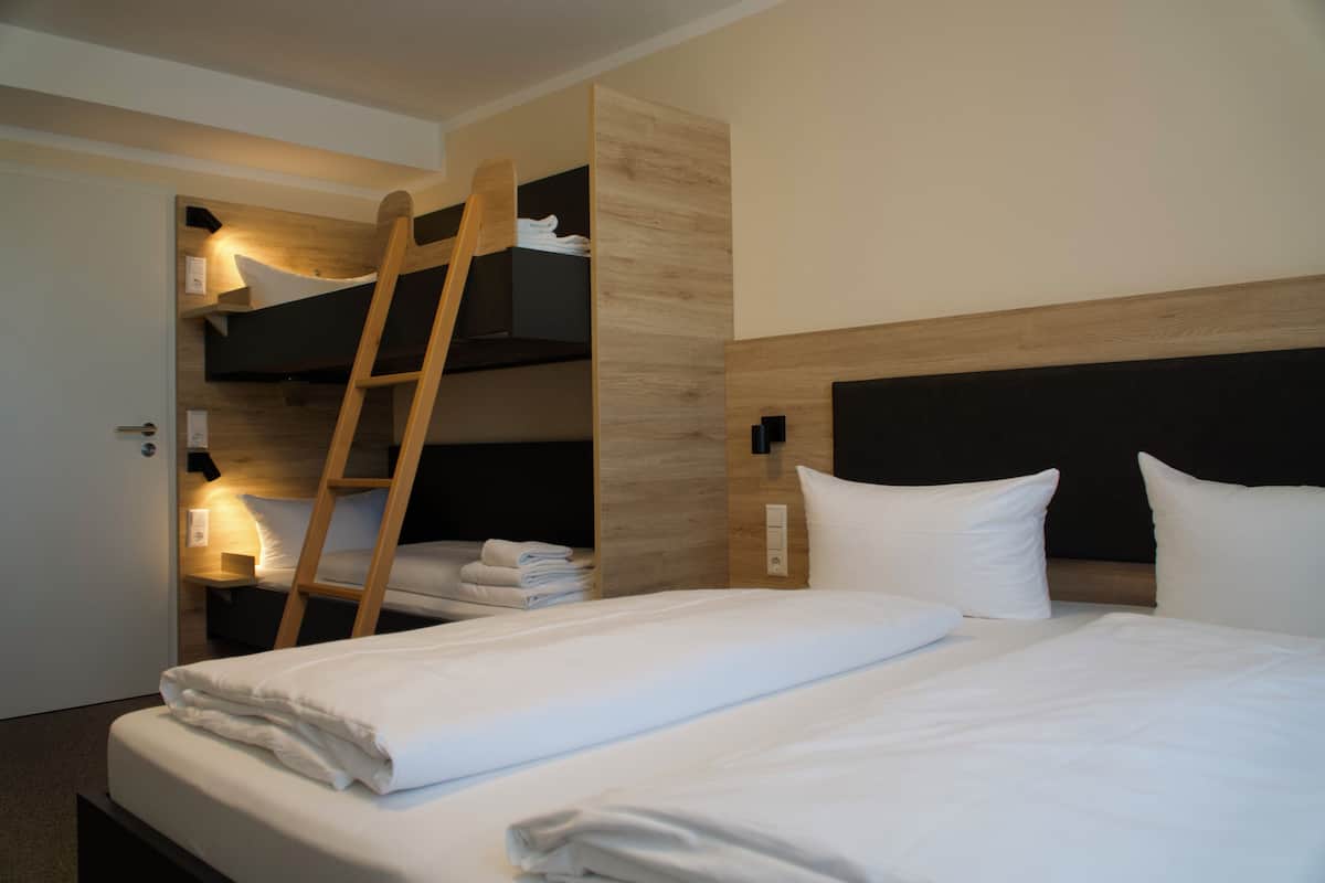 Ein Hotelzimmer mit einem Stockbett, einer Holzleiter, einem Nachttisch mit Lampe und einer Wandleuchte.