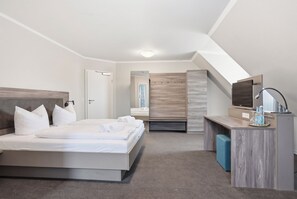 Et moderne hotelværelse med seng, skrivebord, spejl og fjernsyn.