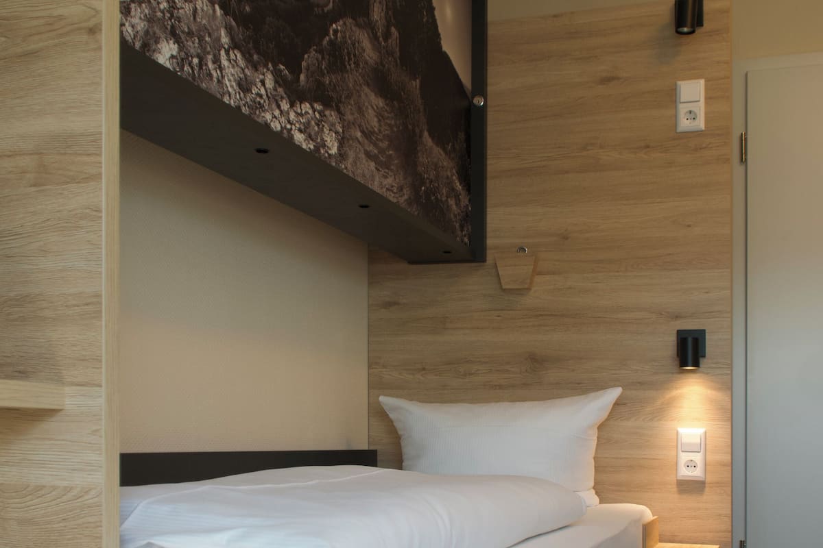 Ein modernes Hotelzimmer mit einem Bett, einem an der Wand befestigten Kunstwerk, einer Wandleuchte und einer Tür.