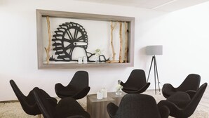A conference room with modern black chairs, a wooden table, a decorative wall piece, and a floor lamp. - Hotel & Tagungszentrum Blaubeuren (Blaubeuren)