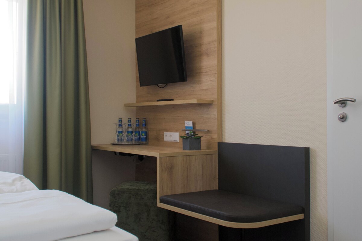 Une chambre d’hôtel comprenant un lit, un bureau avec une chaise, une télévision et une fenêtre avec des rideaux.