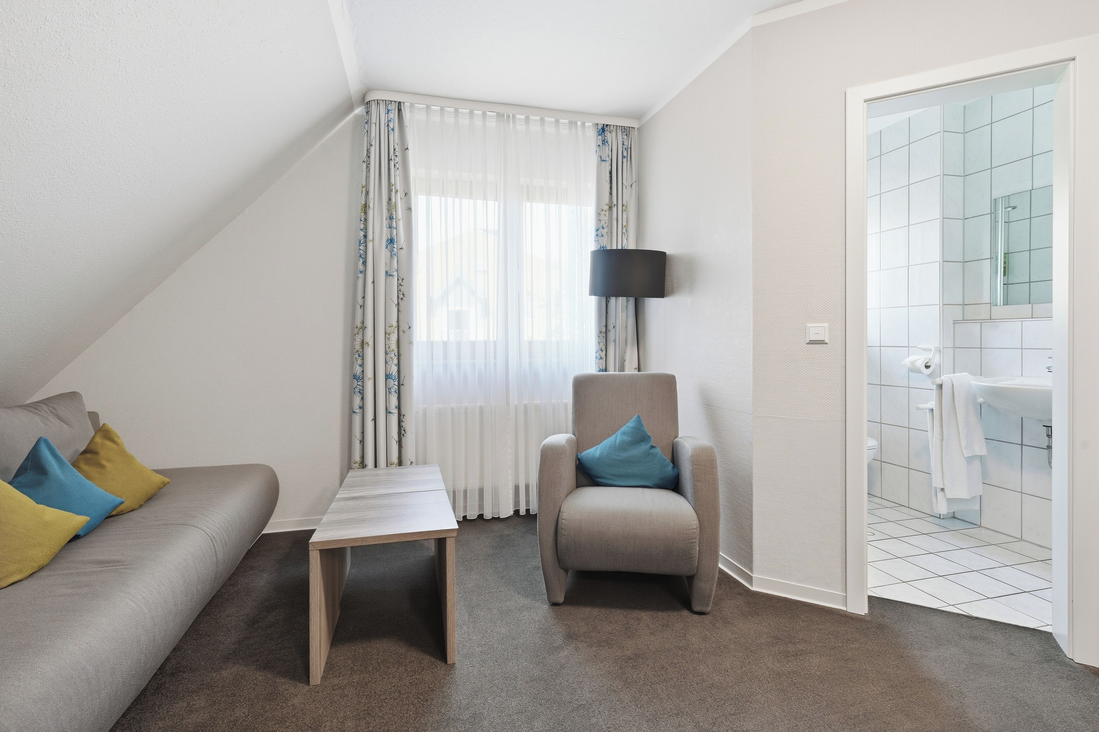 Une pièce moderne et bien éclairée, comprenant un canapé, un fauteuil, une petite table et une salle de bain avec douche et lavabo.