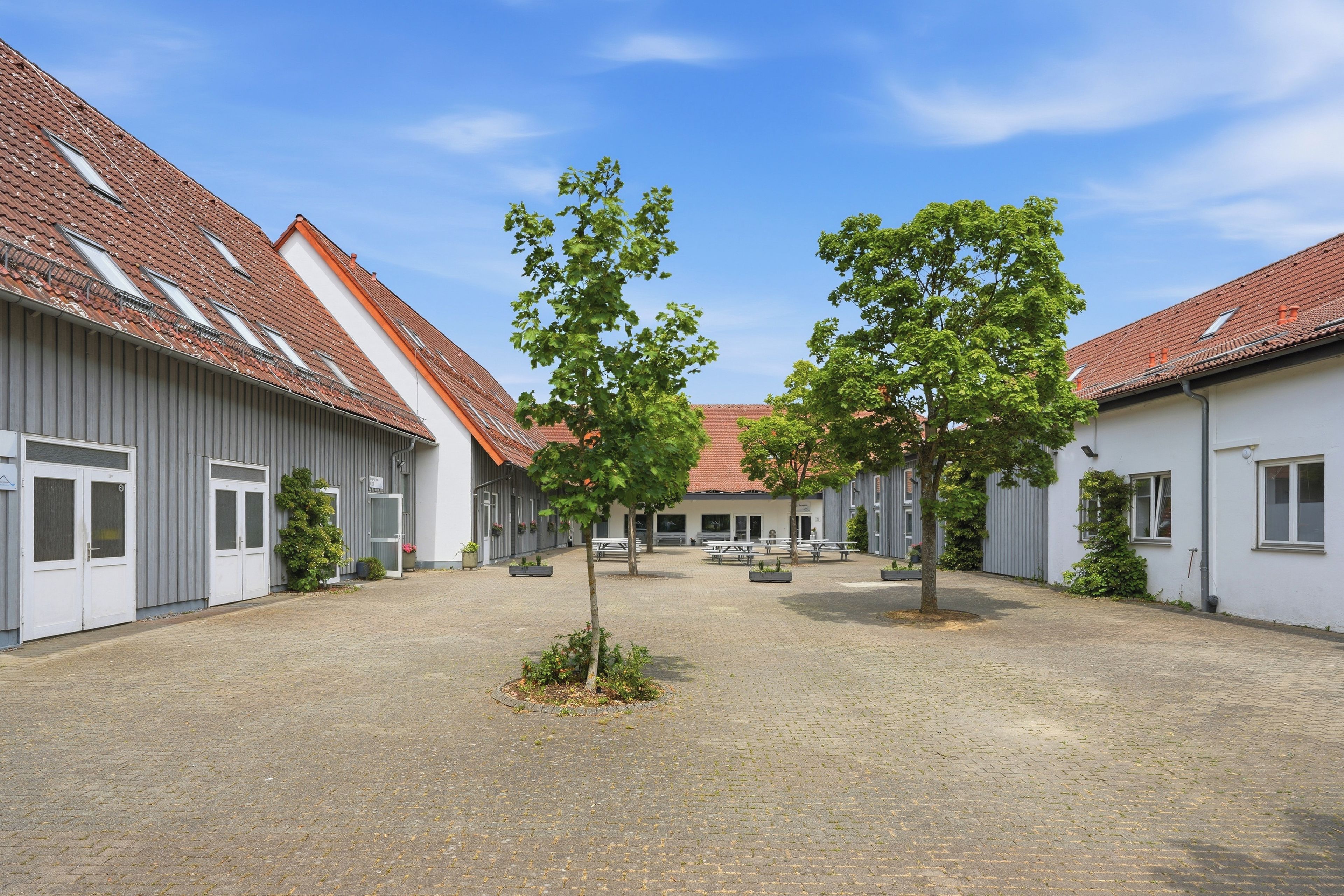 Ein Innenhof mit Gebäuden, Bäumen und Picknicktischen.