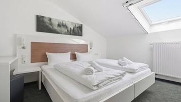 A hotel room with a bed, a nightstand, a wall-mounted lamp, a painting, and a skylight.
