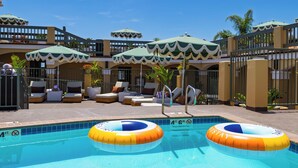 Un espace piscine aménagé avec des chaises longues, des parasols et une piscine équipée de deux bouées gonflables.