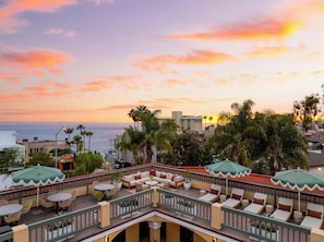 A rooftop terrace with outdoor seating, a view of the ocean, and palm trees.