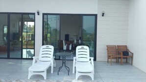 Un área junto a la piscina con dos sillones blancos, una mesita y un banco de madera.