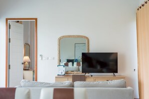 En stue med fjernsyn, et spejl, en sofa og en dør til et andet rum.