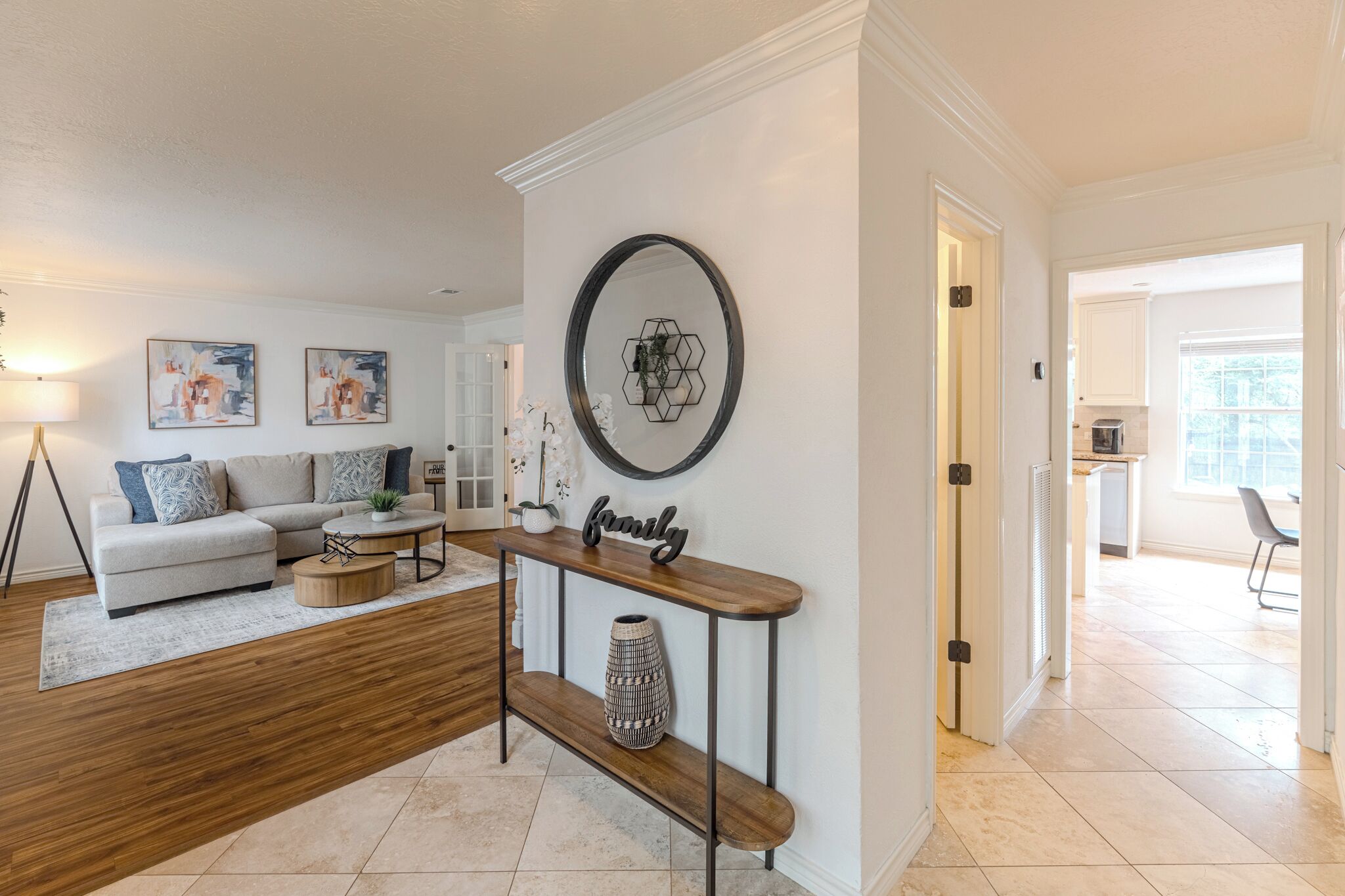 A living room with a sofa, coffee table, and a console table with a vase. There is a wall-mounted mirror and artwork.