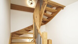 Uma escada espiral de madeira com design moderno, um lustre no teto e uma parede branca.